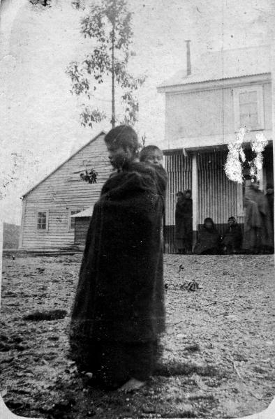 Adolescente indígena caminando con niño colgado a su espalda